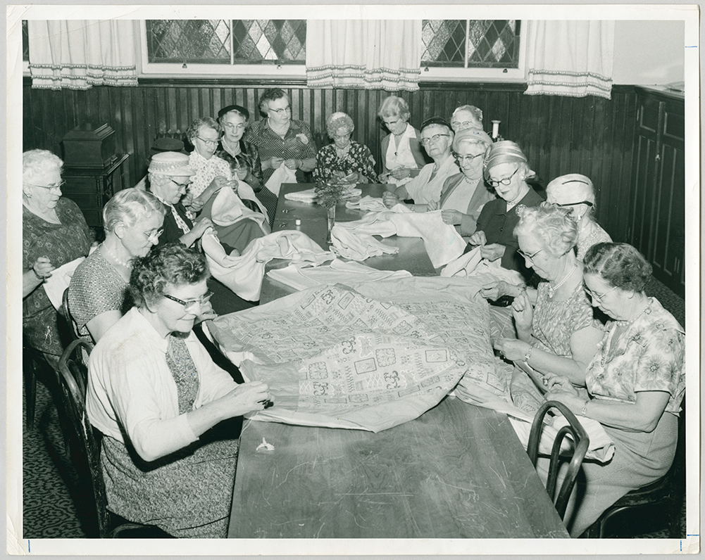 People seated at a table working on a large quilt