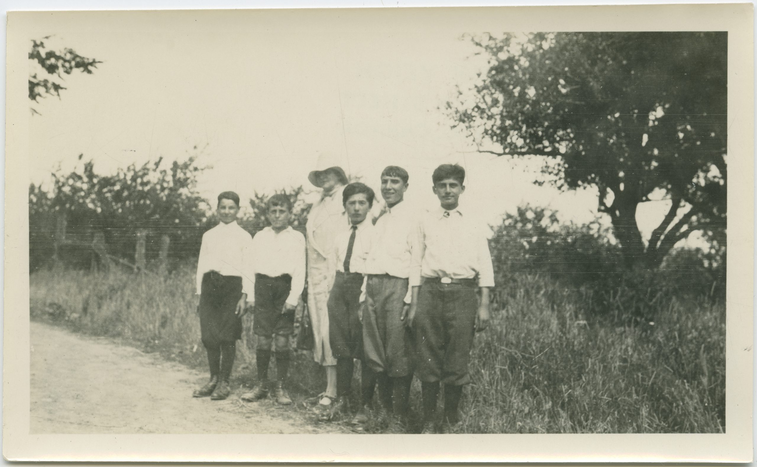 Group people standing on the side of the road with tall grass and trees in the background.