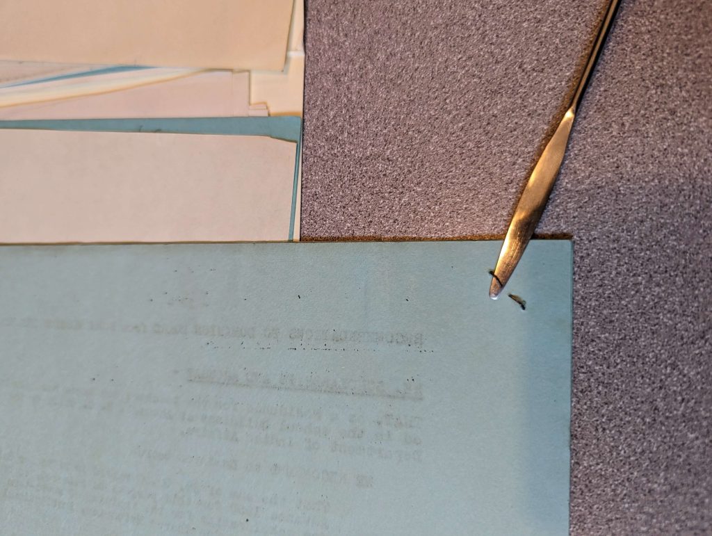 Stack of stapled papers on a grey desk. An instrument to remove staples is being used.