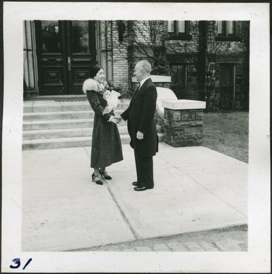 A Korean youth and white adult shake hands by the front steps of a college.
