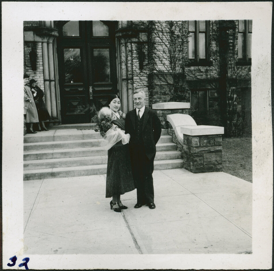A Korean youth and a white adult stand by the front steps of a college.